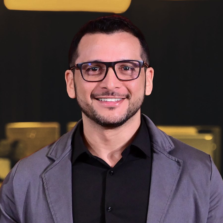 Marcus Cruz, fundador da McTech, sorrindo, de óculos, camisa preta e blazer cinza.